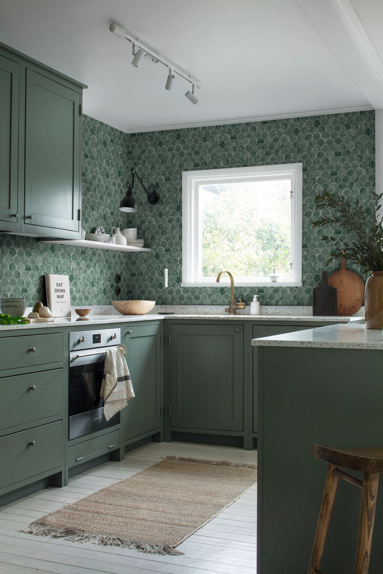 Igor Shells, Pattern Wallpaper in green featured on a wall of a room with a wooden round table with a lamp, books and furnitures 